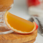 A cored apple slice filled with an apple cider jello shot rests on a small wooden board.