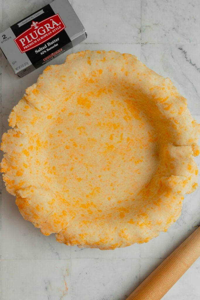 A cheddar cheese pie crust rolled out and fitted into a pie plate.