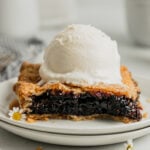 A slice of mulberry slab pie on a white plate topped with a scoop of vanilla ice cream.