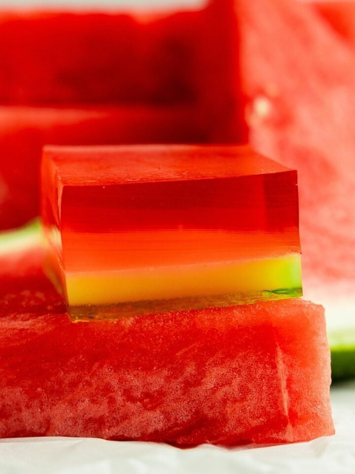 A layered watermelon jello shot sits on a slice of watermelon.
