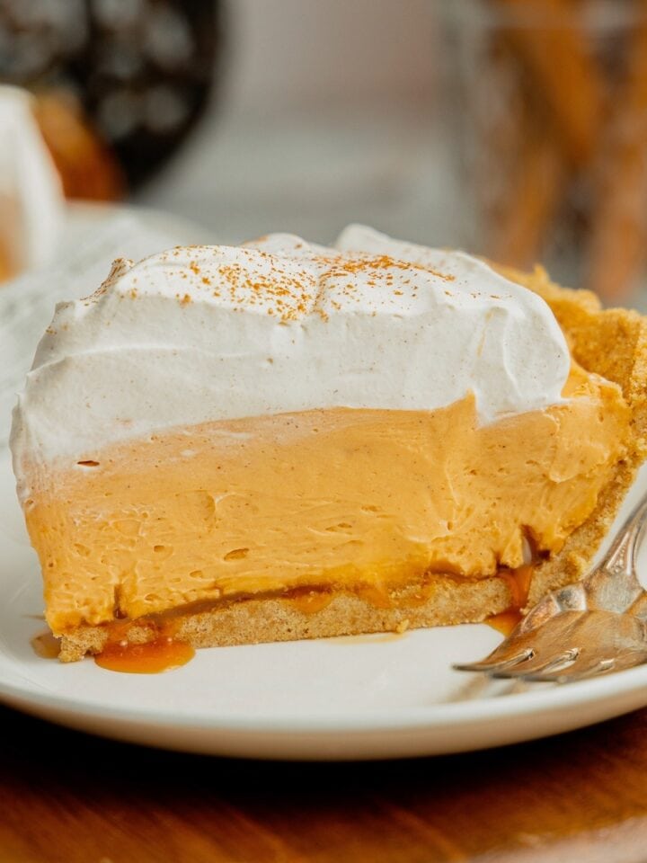 A slice of no bake pumpkin pudding pie with salted caramel and topped with cool whip on a white plate.
