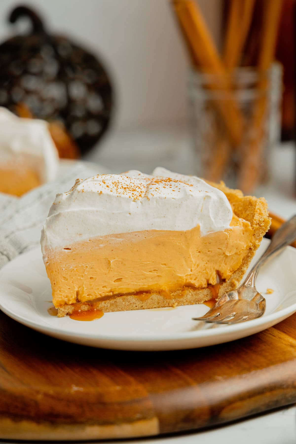 A slice of no bake pumpkin pudding pie with  salted caramel and topped with cool whip on a white plate.
